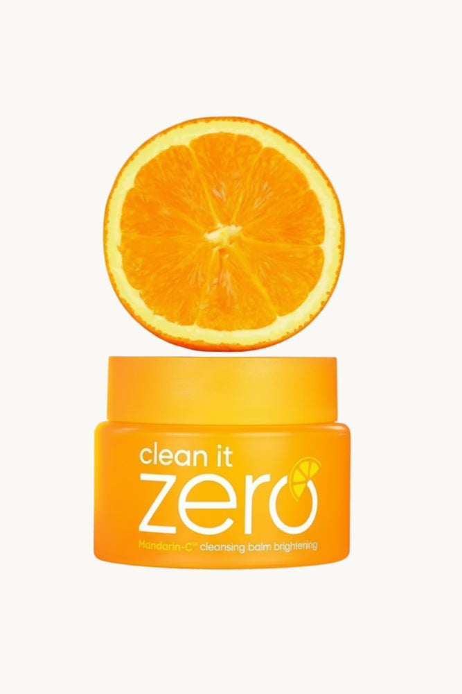 Jar of 'clean it zero' cleansing balm with a sliced orange on an cream background
